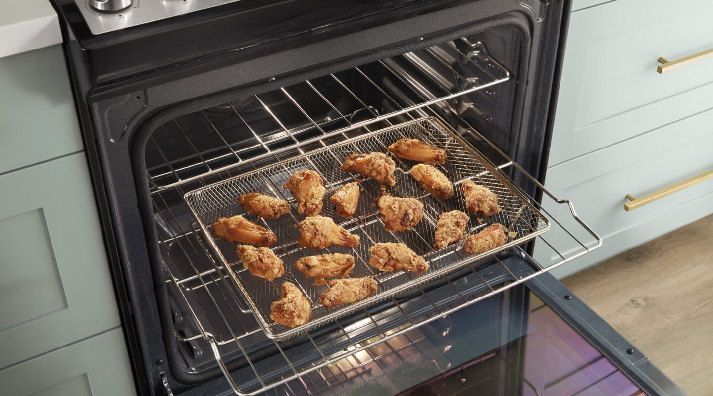 Chicken wings in an air fry basket inside an open oven