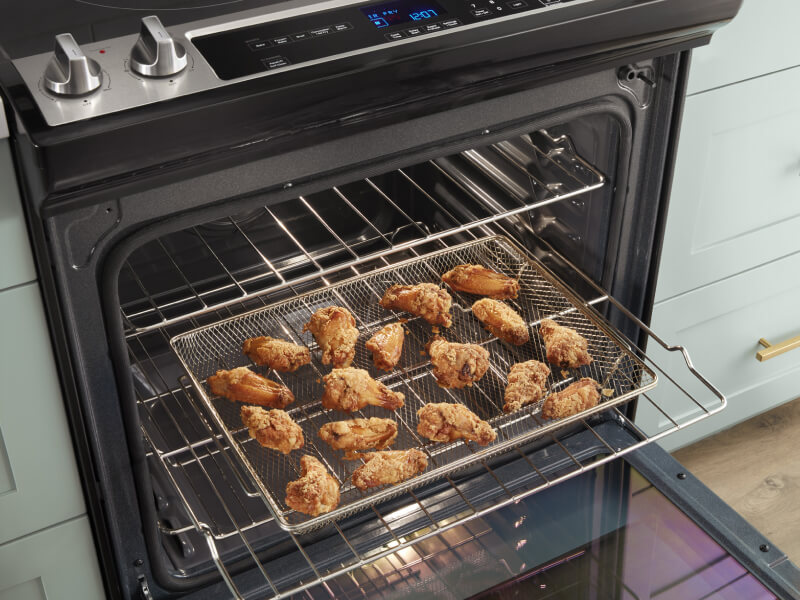 Chicken wings in an air fry basket inside an open oven