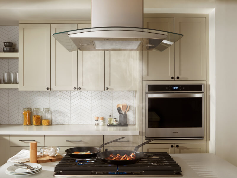 Bacon and eggs simmering on a gas cooktop underneath an island canopy hood