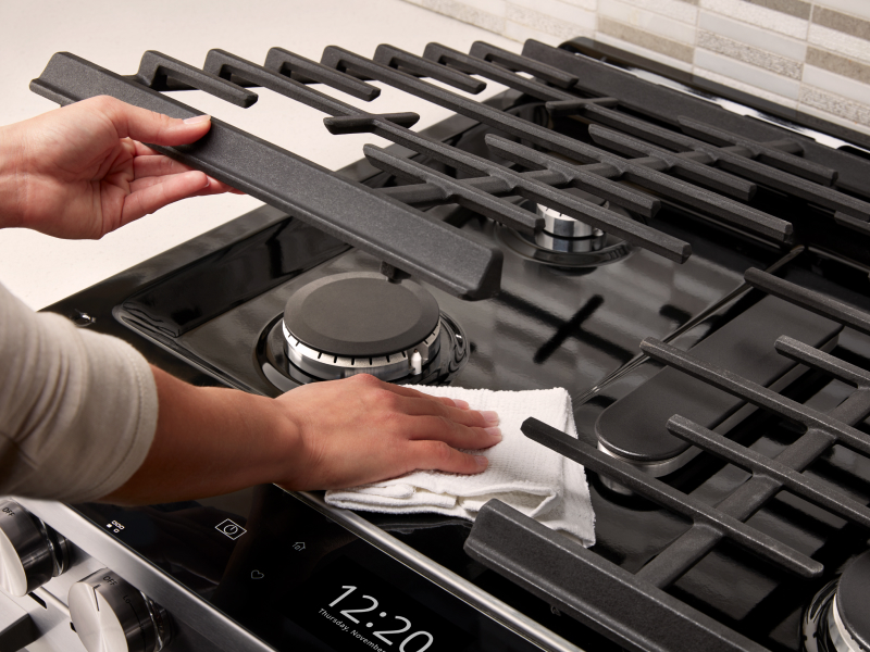 Person wiping underneath a gas cooktop grate