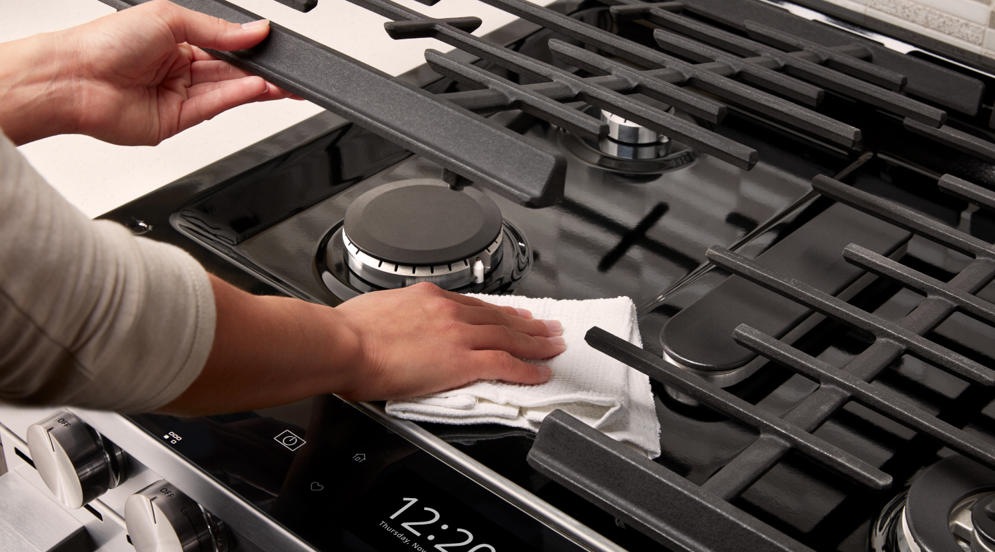 Person wiping underneath a gas cooktop grate