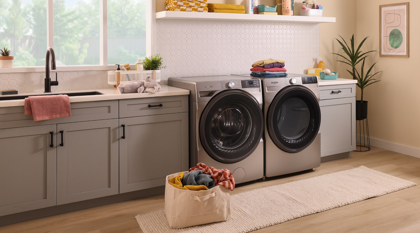 A contemporary laundry room with a utility sink, grey cabinets and side-by-side front load washer and dryer