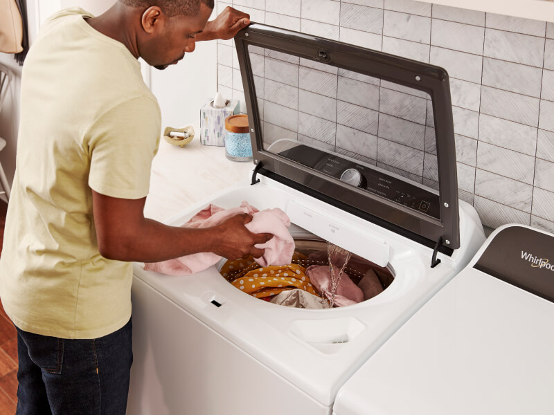 Man in a yellow shirt loading laundry into a top load washing machine from Whirlpool brand
