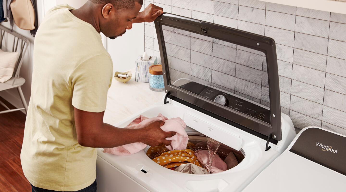 Man in a yellow shirt loading laundry into a top load washing machine from Whirlpool brand