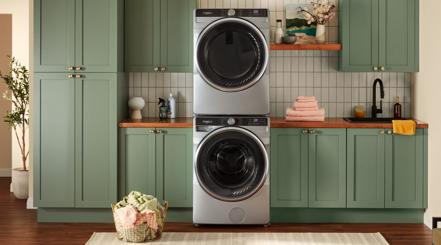 Stacked front load washer and dryer surrounded by green cabinets