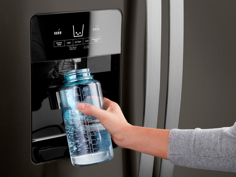 Person using an in-door water dispenser on a fridge to fill a water bottle