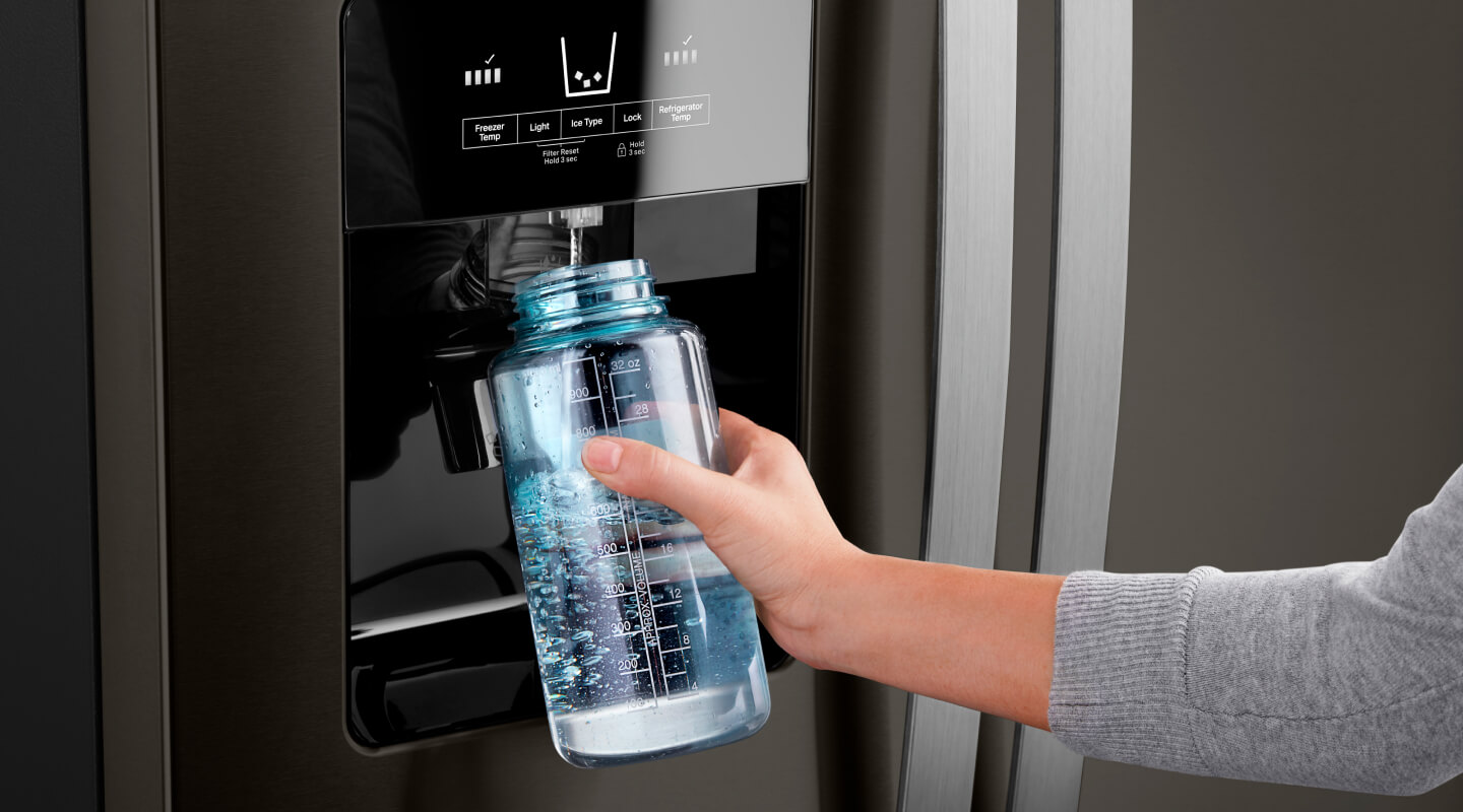 Person using an in-door water dispenser on a fridge to fill a water bottle
