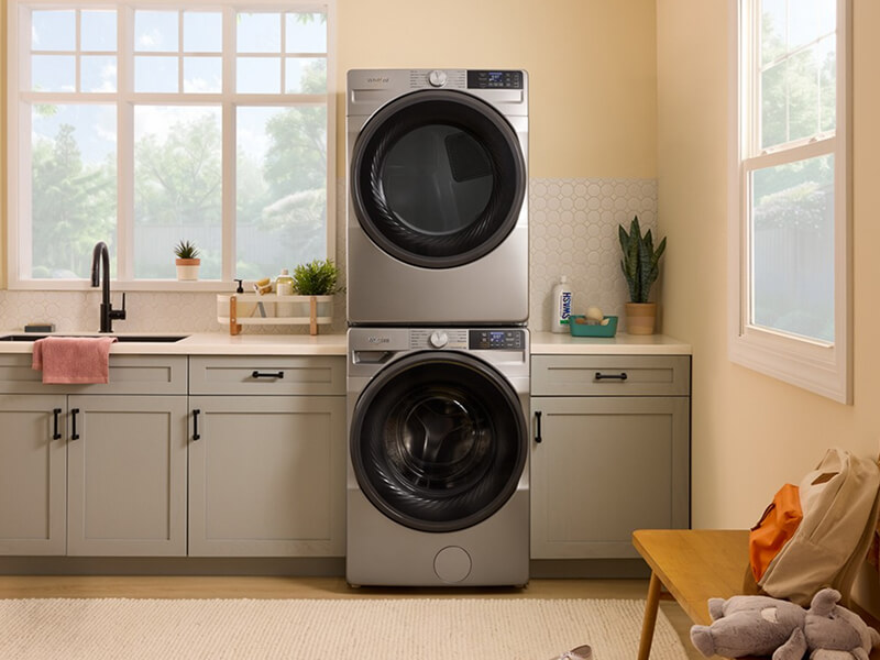 Stainless steel front load washer and dryer in a laundry room with gray cabinetry