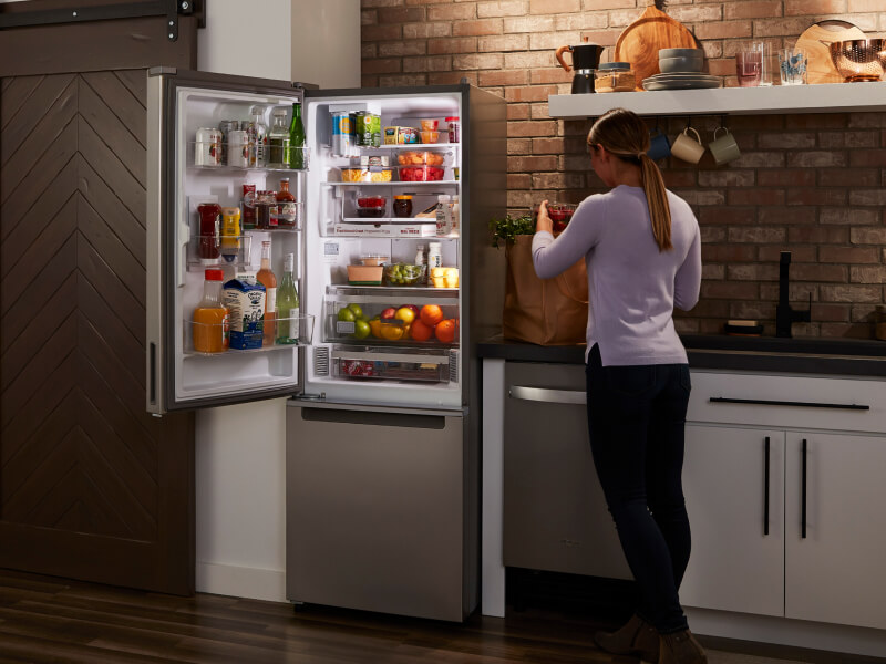 Person standing in front of an open stainless steel Whirlpool® bottom freezer fridge