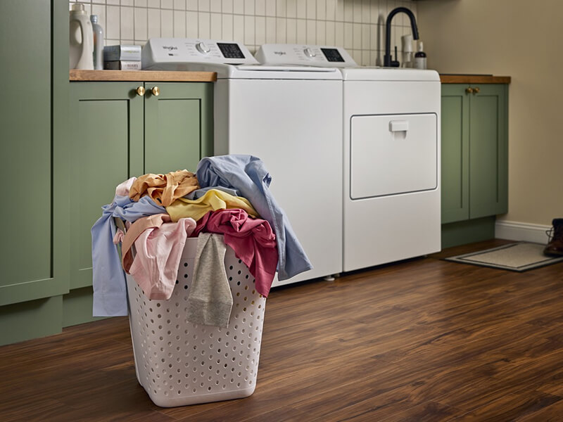 A basket of laundry in front of a washer and dryer set in a laundry room