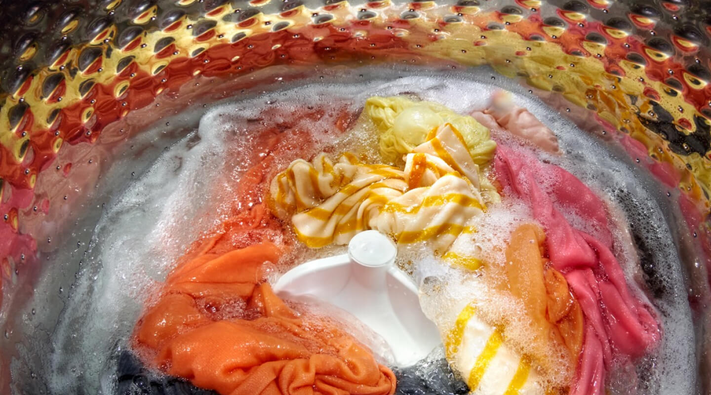 Interior of a Whirlpool® Washer with an impeller washing yellow, orange, pink, gray and white garments