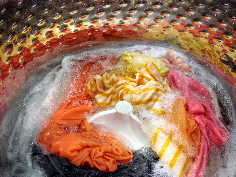 Interior of a Whirlpool® Washer with an impeller washing yellow, orange, pink, gray and white garments