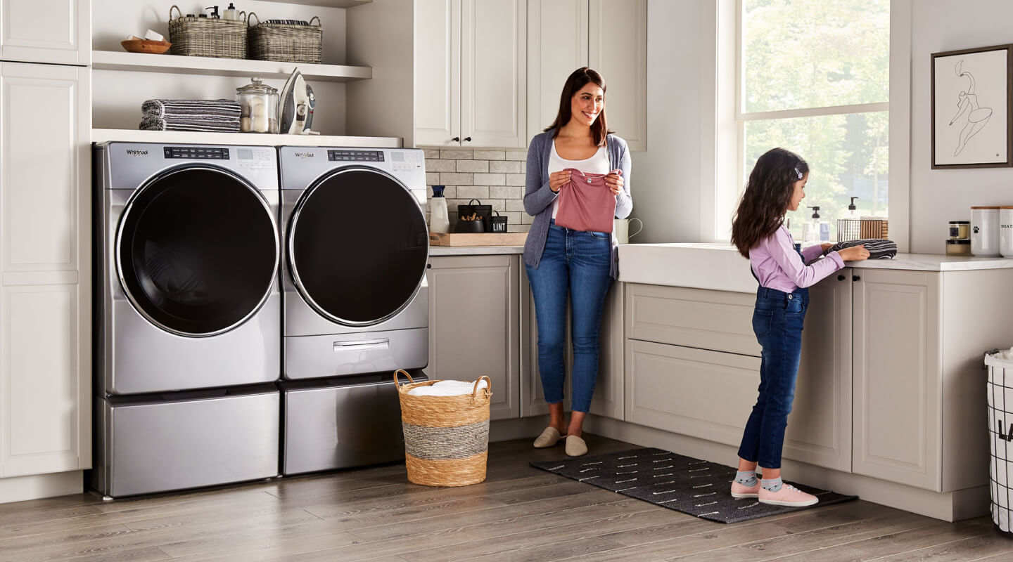 A parent and child in a laundry room with a Whirlpool® Front-Load Washer and Dryer set