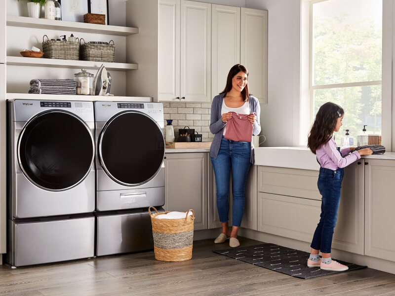 A parent and child in a laundry room with a Whirlpool® Front-Load Washer and Dryer set