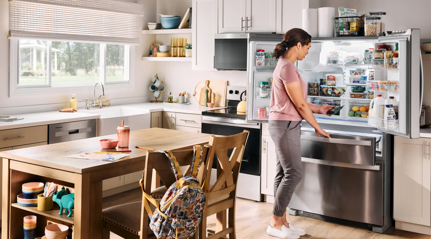 A person in front of an open Whirlpool® refrigerator in a kitchen