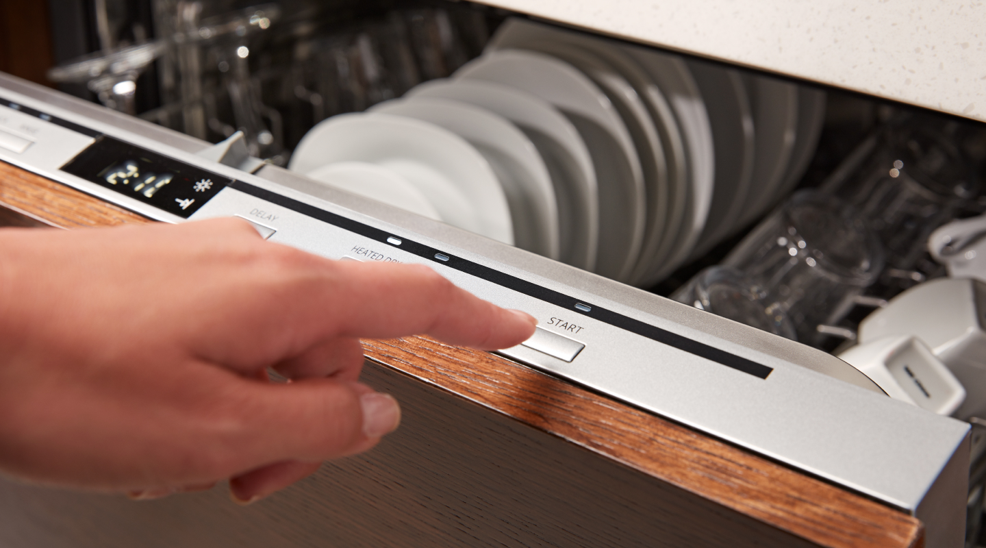 A person starting a dishwasher cycle on a top control panel.
