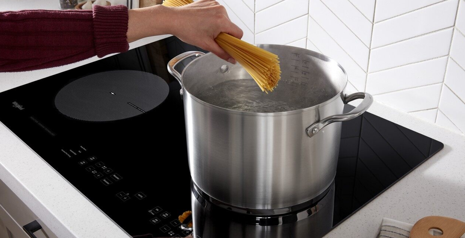 A hand putting spaghetti into pot of boiling water on a Whirlpool® Induction Cooktop