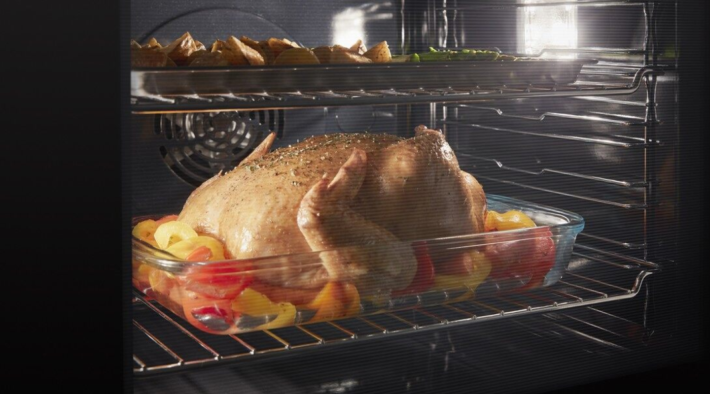 Closed oven with oven light on showing dual racks of elaborate dishes cooking