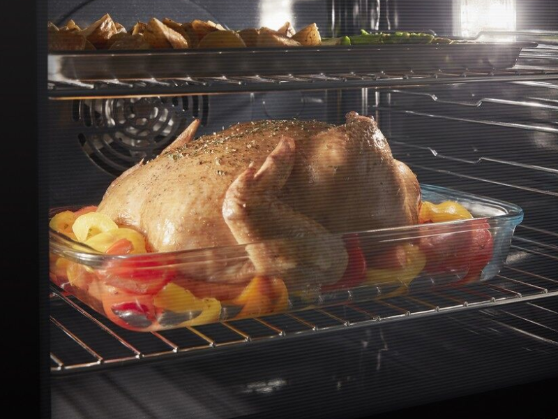 Closed oven with oven light on showing dual racks of elaborate dishes cooking