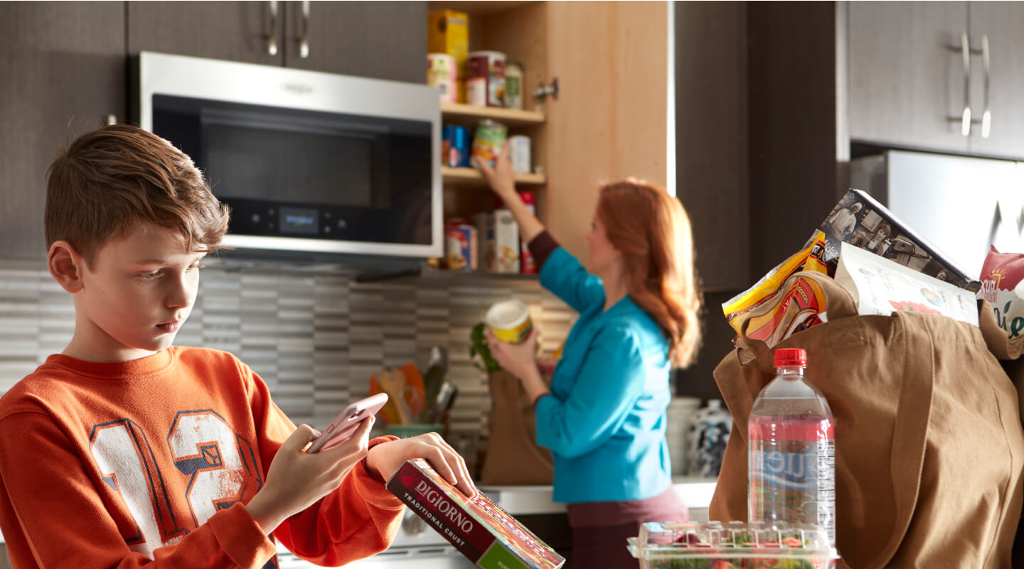 A person scanning a pizza box barcode while a person in the background puts items in the cabinet