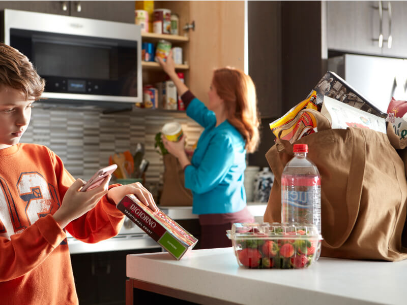 A person scanning a pizza box barcode while a person in the background puts items in the cabinet