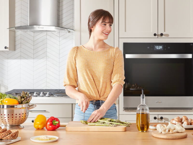 A person chopping asparagus on a wooden cutting board placed on a kitchen island with a cooktop in the background behind her