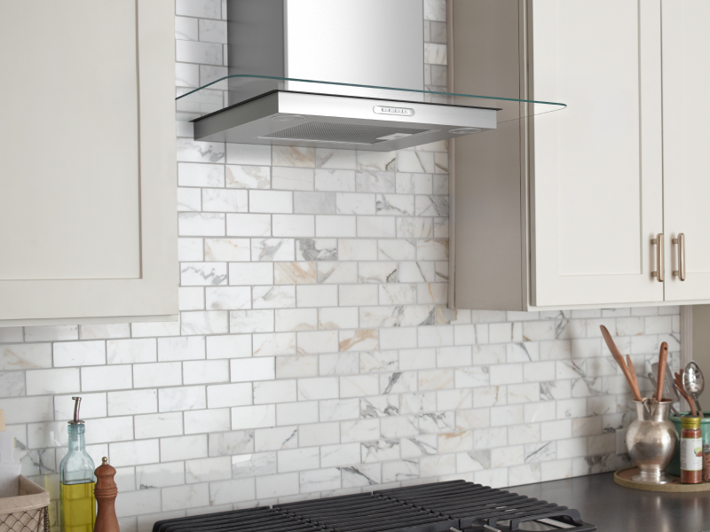 Stainless steel range hood between white cabinetry