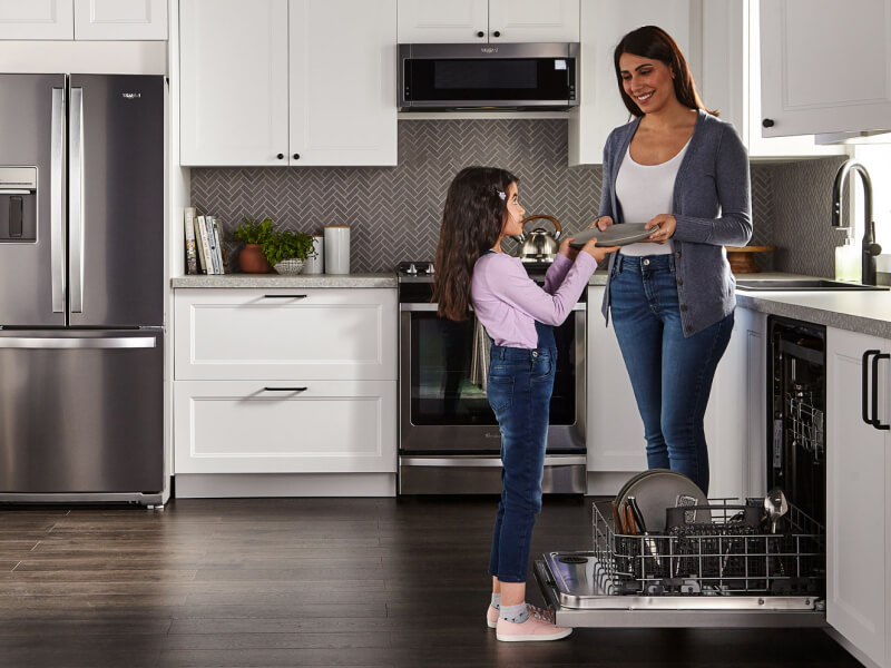 Person handing a child a clean dish next to a dishwasher