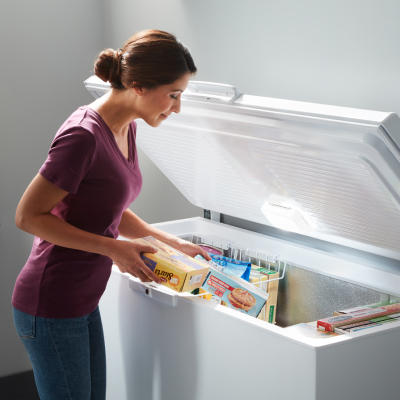 A woman placing frozen groceries into a white chest freezer