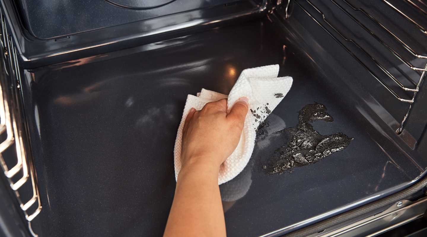 Hand holding paper towel wiping residue off of bottom of oven cavity