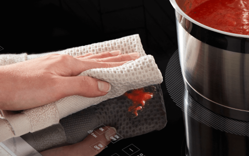 Person cleaning a Whirlpool® induction cooktop with a towel