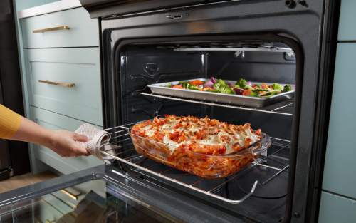 An open oven with baked ziti and vegetables on different racks
