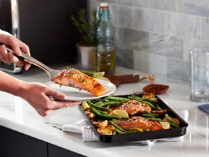 Person plating a salmon filet from a sheet pan of vegetables and salmon